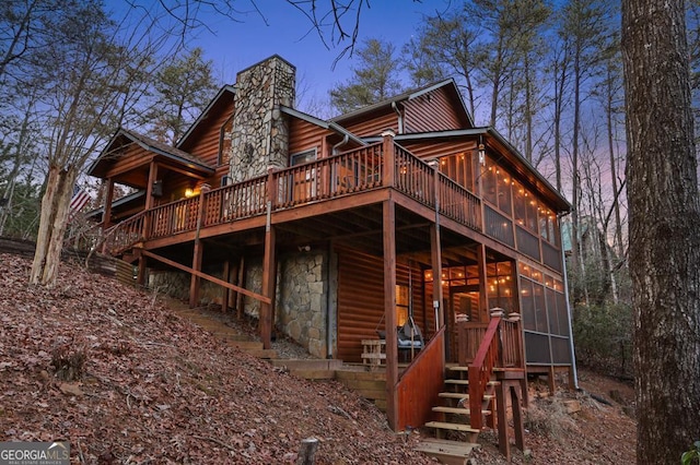 back of house featuring a sunroom, a chimney, and a wooden deck