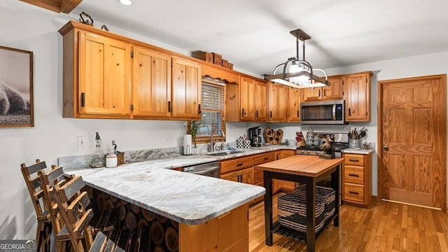 kitchen with a peninsula, hanging light fixtures, stainless steel appliances, light wood-style floors, and a sink