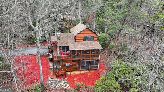 rear view of property with a shingled roof, faux log siding, a view of trees, and a wooden deck