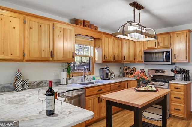 kitchen featuring appliances with stainless steel finishes, decorative light fixtures, light stone countertops, light wood-type flooring, and a sink