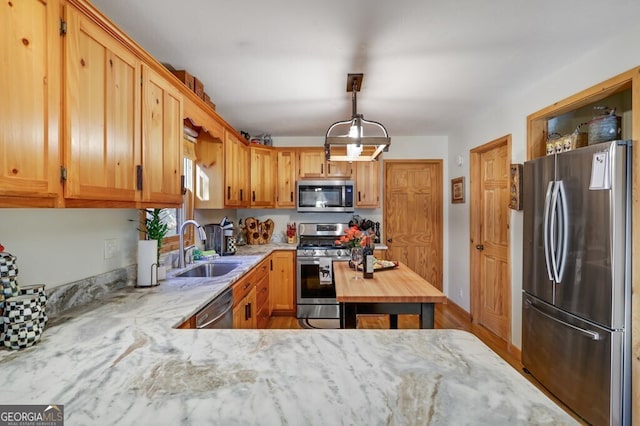 kitchen featuring light stone counters, stainless steel appliances, a sink, and decorative light fixtures