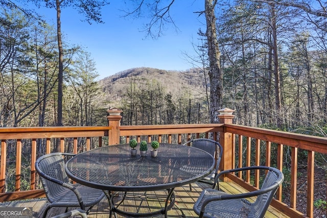 wooden deck with outdoor dining area, a mountain view, and a wooded view