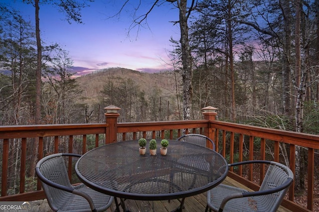 deck at dusk with a forest view, a mountain view, and outdoor dining space