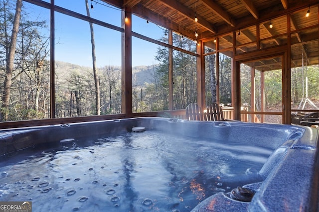 unfurnished sunroom featuring beamed ceiling, wood ceiling, and a view of trees