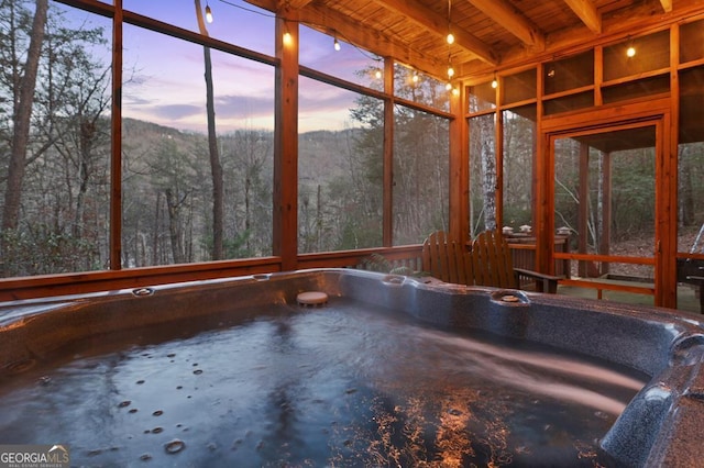 unfurnished sunroom featuring a forest view, wooden ceiling, and beam ceiling