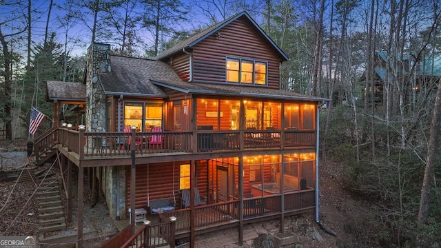 rear view of property with log veneer siding, a sunroom, a chimney, roof with shingles, and stairs