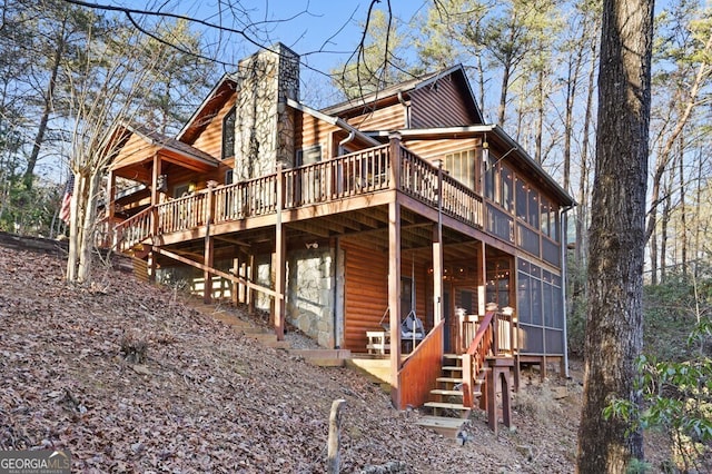 rear view of property featuring a deck, a sunroom, and a chimney