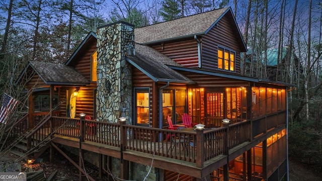 back of house with a chimney, log veneer siding, a deck, and roof with shingles