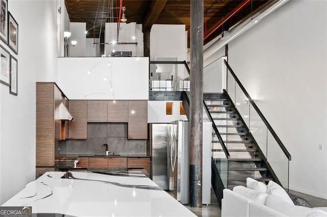 kitchen featuring sink, tasteful backsplash, hanging light fixtures, stainless steel fridge, and a high ceiling