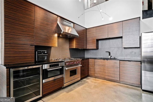 kitchen featuring appliances with stainless steel finishes, sink, beverage cooler, backsplash, and wall chimney exhaust hood