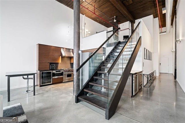 staircase featuring a towering ceiling, beverage cooler, and concrete flooring