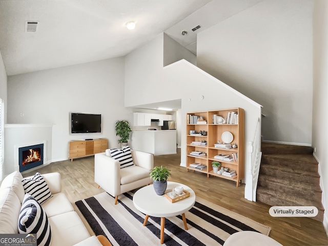 living room featuring high vaulted ceiling, visible vents, a lit fireplace, stairway, and light wood-type flooring