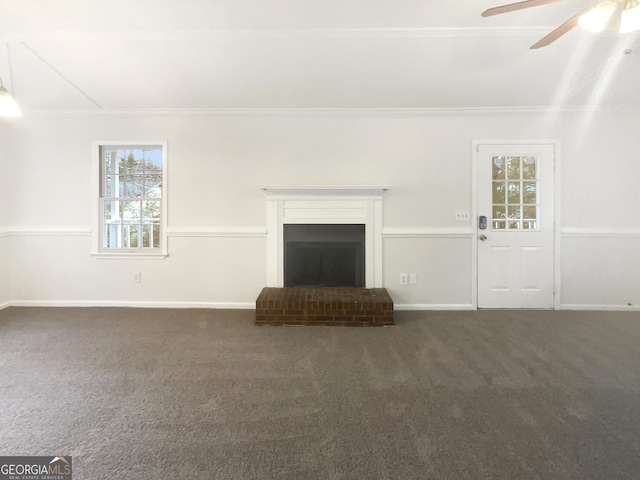 unfurnished living room with crown molding, a brick fireplace, dark carpet, and ceiling fan