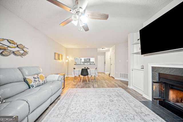 3655 Habersham Rd Unit B129, Atlanta, GA 30305 - living room featuring a tiled fireplace, wood-type flooring, a textured ceiling, and ceiling fan