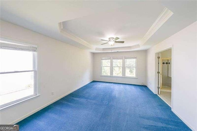 unfurnished room with a raised ceiling, crown molding, ceiling fan, and dark carpet