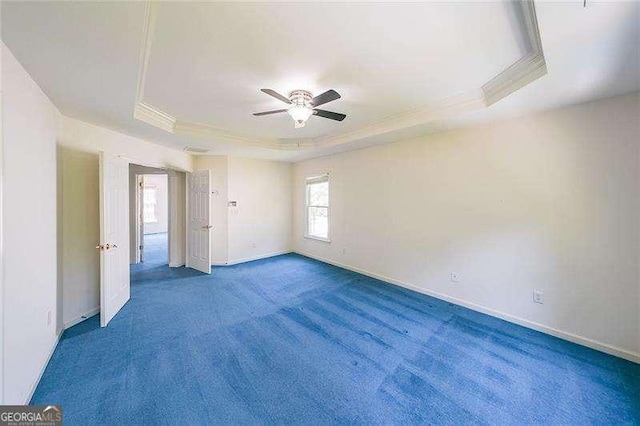 empty room with a raised ceiling, crown molding, carpet floors, and ceiling fan