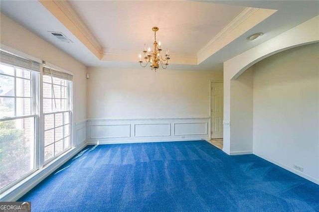 carpeted empty room featuring an inviting chandelier, ornamental molding, and a tray ceiling