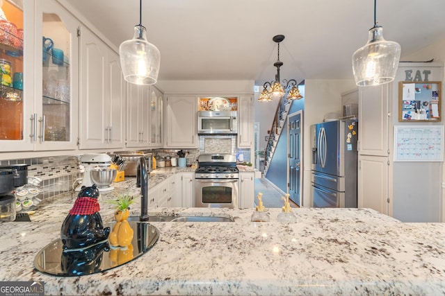 kitchen with appliances with stainless steel finishes, white cabinetry, sink, decorative backsplash, and hanging light fixtures