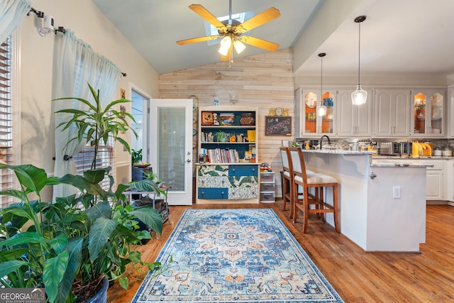 kitchen featuring a breakfast bar, white cabinetry, hanging light fixtures, light stone counters, and light hardwood / wood-style floors