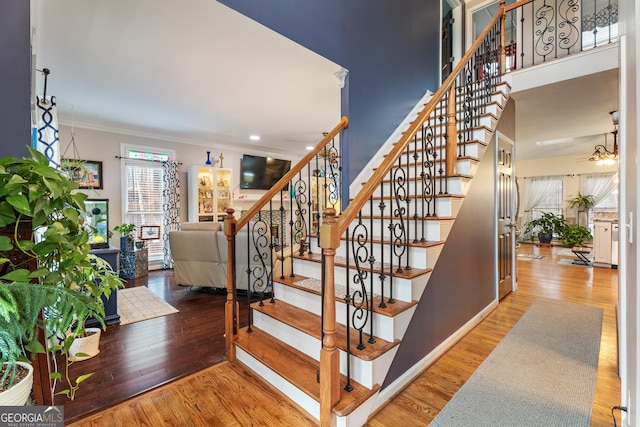 stairway featuring crown molding, ceiling fan, hardwood / wood-style floors, and a towering ceiling