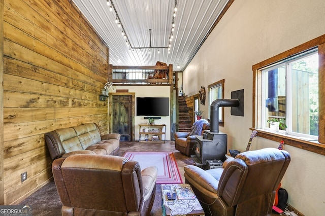 living room with a high ceiling, a wood stove, track lighting, and wooden walls