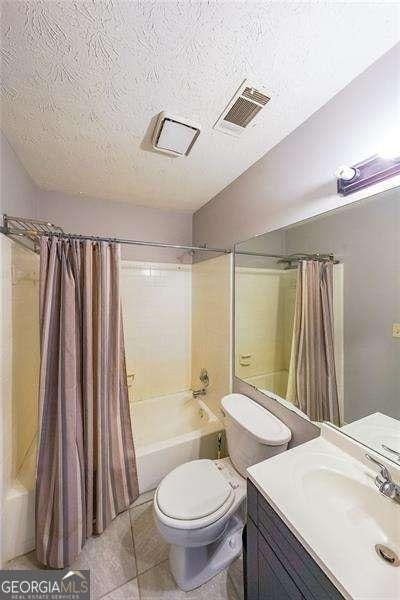 full bathroom with shower / tub combo, vanity, a textured ceiling, tile patterned floors, and toilet