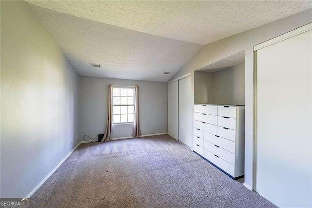 unfurnished bedroom with lofted ceiling, light colored carpet, a textured ceiling, and two closets