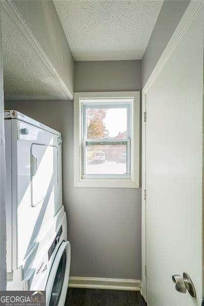 washroom featuring dark hardwood / wood-style floors, stacked washer and clothes dryer, and a textured ceiling