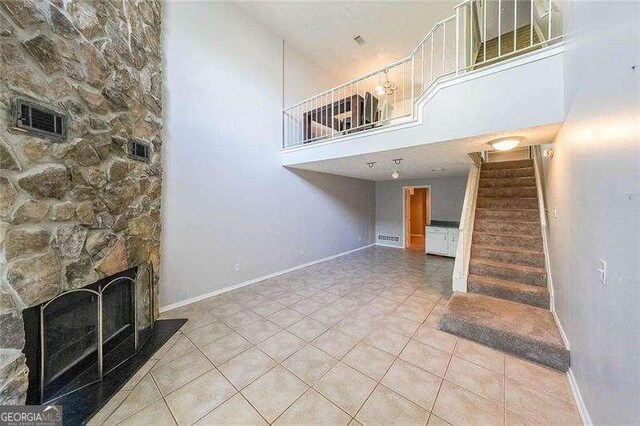 unfurnished living room featuring a stone fireplace, tile patterned floors, and a high ceiling