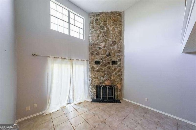 unfurnished living room with light tile patterned flooring, a towering ceiling, and a fireplace