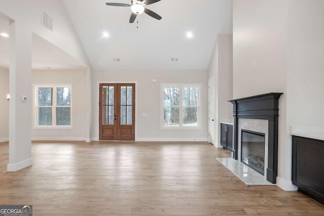 unfurnished living room featuring a premium fireplace, plenty of natural light, high vaulted ceiling, and light hardwood / wood-style floors