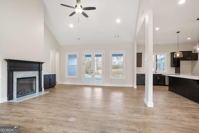 unfurnished living room featuring ceiling fan, high vaulted ceiling, a fireplace, french doors, and light wood-type flooring