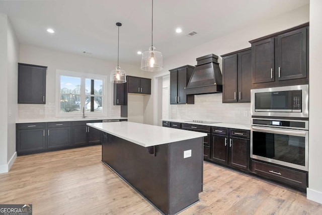 kitchen with premium range hood, a kitchen island, hanging light fixtures, light hardwood / wood-style floors, and stainless steel appliances