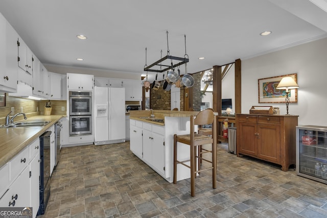 kitchen with a center island, white refrigerator with ice dispenser, stainless steel double oven, white cabinetry, and a sink