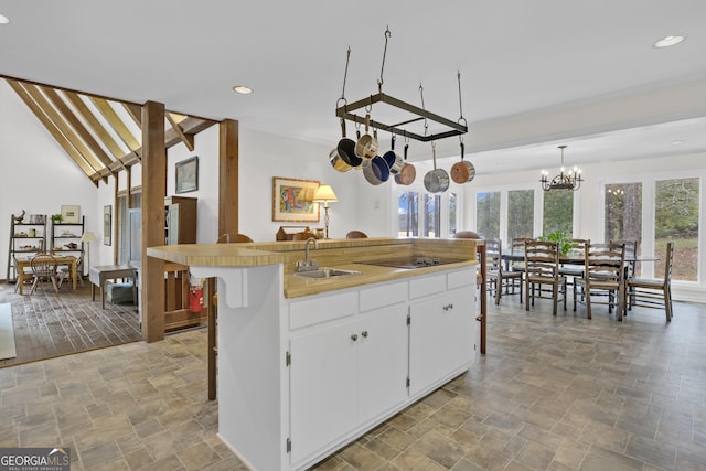 kitchen featuring a sink, white cabinetry, stone finish flooring, an island with sink, and pendant lighting