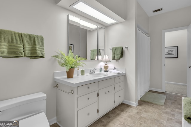 bathroom featuring a skylight, baseboards, visible vents, toilet, and vanity