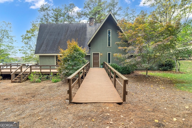 view of front facade featuring roof with shingles, a chimney, and a wooden deck