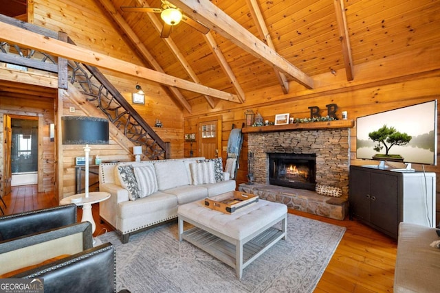 living room with a stone fireplace, wood ceiling, wood-type flooring, wooden walls, and beamed ceiling