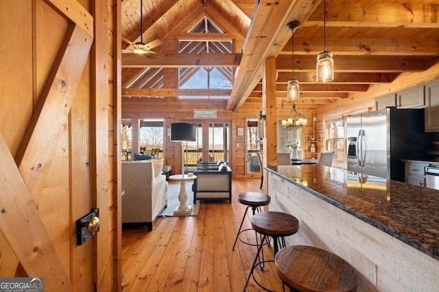 kitchen featuring pendant lighting, stainless steel fridge with ice dispenser, light wood-type flooring, dark stone counters, and wood walls