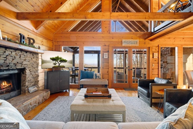 living room featuring light hardwood / wood-style flooring, a stone fireplace, french doors, beamed ceiling, and wood walls