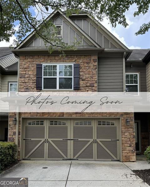 view of front facade featuring a garage, driveway, board and batten siding, and stone siding