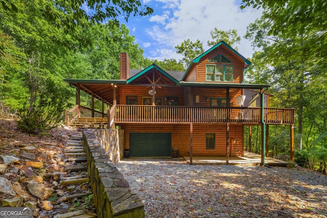 rear view of house featuring a garage, a chimney, a wooden deck, log veneer siding, and gravel driveway