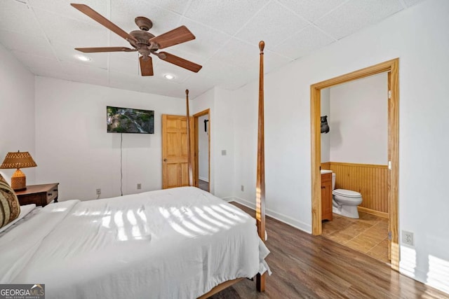 bedroom with wood walls, dark hardwood / wood-style flooring, ensuite bath, and a drop ceiling