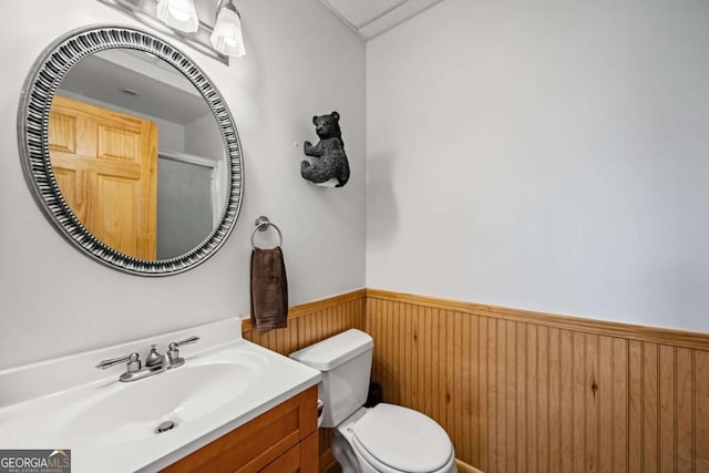 bathroom with vanity, wooden walls, and toilet