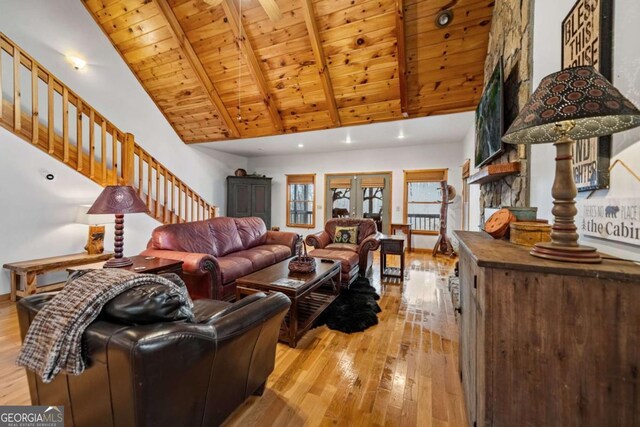 living room featuring hardwood / wood-style floors, beam ceiling, a stone fireplace, wooden ceiling, and french doors