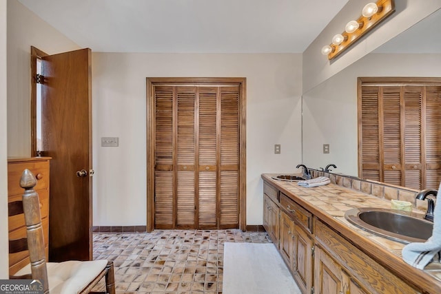 bathroom featuring a sink, double vanity, baseboards, and a closet