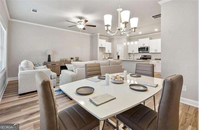 dining area featuring ceiling fan with notable chandelier, visible vents, baseboards, light wood finished floors, and crown molding