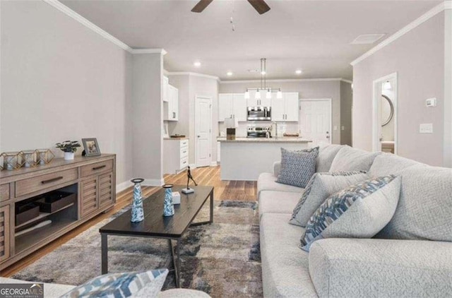 living room featuring ceiling fan, light wood-style flooring, recessed lighting, baseboards, and crown molding