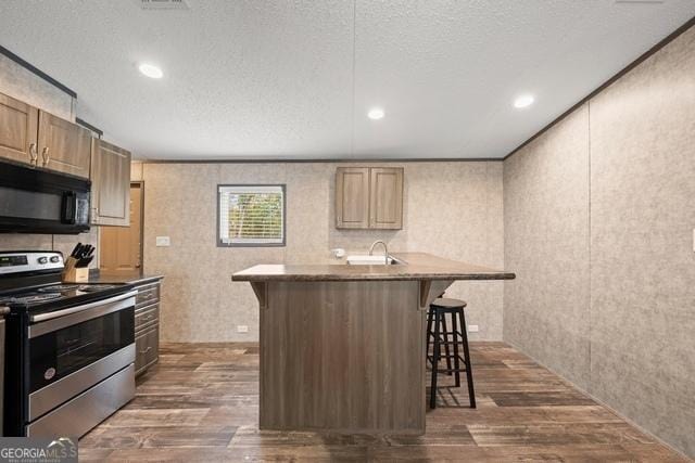 kitchen with black microwave, dark wood-style flooring, a kitchen bar, and stainless steel range with electric stovetop