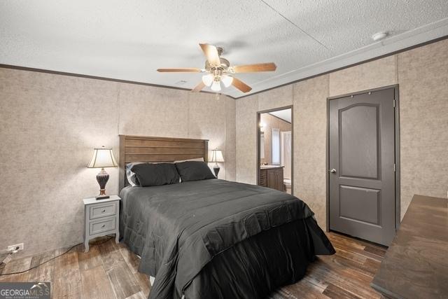 bedroom with ceiling fan, a textured ceiling, ensuite bathroom, wood finished floors, and ornamental molding